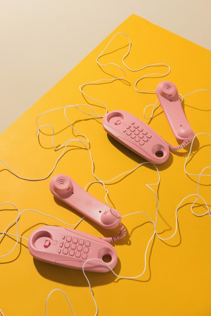 Due telefoni rosa a filo poggiati su un ripiano giallo: una buona metafora di un servizio clienti aperto e disponibile