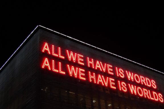 Scritta al neon rossa: "All we have is words, all we have is worlds"